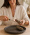 Woman lighting a Yerba Santa, Lavender & Blue Sage cleansing bundle over a dark stone dish