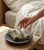 Hand reaching for the Cleansing Bundle Trio on a stone dish on a bedside table