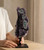 Hands setting a Black Amethyst cluster on its iron stand onto a wooden table