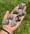 Seven Labradorite sleeping cat carvings in a palm, showing the natural range from light gray to dark charcoal