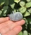 Side view of a gray Labradorite sleeping cat carving held between fingers, about 1 inch long