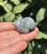Labradorite sleeping cat carving with a dark tail patch, resting curled up on fingertips