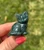 Polished Moss Agate sitting cat carving from Brazil in deep green with darker moss patterns, held between fingers