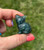 Moss Agate sitting cat figurine held between thumb and finger, showing its pointed ears and curled tail