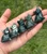 Five Moss Agate sitting cats lined up in a palm, from deep forest green to mottled white, gray and green