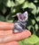 Amethyst sitting cat held in hand against green leaves, about 1.25 inches tall, with pale lilac ears