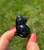 Side view of a Smoky Quartz sitting cat held between fingertips, showing its rounded back