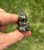 Pyrite sitting cat figurine held between fingertips, showing its pointed ears and metallic speckles
