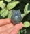 Polished Labradorite owl carving from Madagascar held in hand, gray with soft blue flash across its carved feathers
