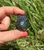 Dark Labradorite owl held between fingertips against green grass, with carved eyes and ear tufts