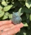 Pale Labradorite owl held in hand against green leaves, glowing with blue labradorescence