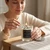 Woman lighting the Winter crystal candle with a match at a wooden table, silver lid resting beside the jar