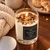 Lit Warm & Cozy snickerdoodle crystal candle on a wooden table with cookies, a coffee mug and a cream knit blanket