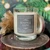 Warm & Cozy crystal candle on a wood slice with gold dried botanicals, evergreen branches and twinkling holiday lights