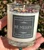 Hand holding Be Merry crystal candle outdoors, crystals, rose petals and herbs visible at the top of the jar