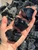 Three large raw black obsidian chunks in a palm over a bin of rough obsidian, with chipped glassy faces catching the light