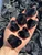 Six rough black obsidian pieces resting in a hand above bulk raw obsidian, with jagged edges and a deep black glassy shine