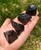 Raw black obsidian chunks lined up across a hand outdoors, each rough stone with a shiny glass-like surface and unique shape