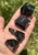 Close-up of raw black obsidian stones in a hand on grass, highlighting smooth glassy faces and rough natural edges of this volcanic glass