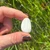 Single teardrop-shaped Scolecite Tumbled Stone held between two fingers, white with fine parallel fibrous lines
