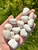 White Scolecite Tumbled Stones in an open hand over green grass, polished rounded and teardrop shapes from India