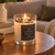 Lit Winter Forest Candle glowing in a glass jar on a wooden side table in a cozy living room