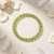Peridot 4mm bead bracelet on cream fabric with white flower petals and clear quartz points