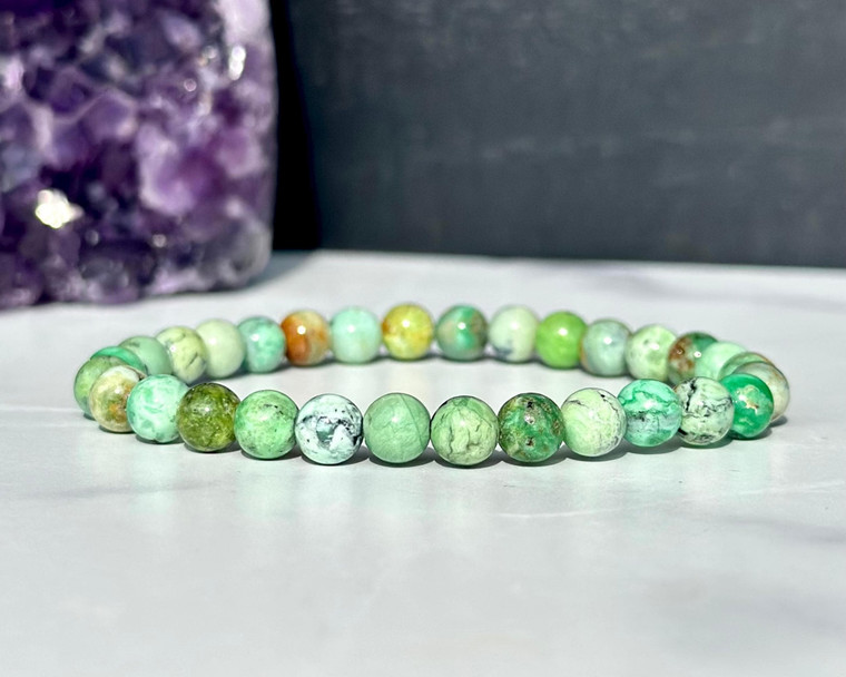 Variscite elastic bracelet with 6mm mint green beads on a white surface in front of an amethyst cluster