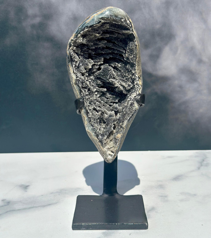 Uruguayan Black Amethyst cluster on a black iron stand with deep ridged charcoal druzy crystals, against a misty backdrop
