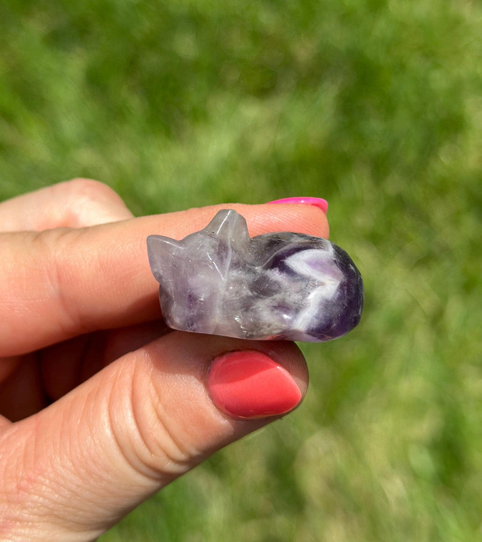 Polished Amethyst sleeping cat carving from Brazil held between fingers, showing purple and white chevron banding