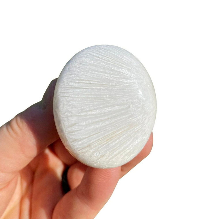 Scolecite palm stone held in hand, a polished white oval showing its radiating needle-like fibrous pattern