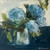 Elegant blue hydrangea canvas wall art by Shakia Harris featuring expressive impressionistic florals in layered shades of soft blue, navy, sage green, and ivory. This floral still life canvas print showcases painterly hydrangeas arranged in a glass vase against a moody dark background, creating a calm and sophisticated atmosphere. Styled in a modern neutral interior, the artwork highlights premium features including water-resistant protection, fade-resistant archival inks, and a textured canvas finish. Perfect for bedrooms, living rooms, entryways, and modern organic interiors seeking soft color, timeless floral elegance, and elevated statement artwork.