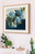 Elegant blue hydrangea canvas wall art by Shakia Harris featuring expressive impressionistic florals in layered shades of soft blue, navy, sage green, and ivory. This floral still life canvas print showcases painterly hydrangeas arranged in a glass vase against a moody dark background, creating a calm and sophisticated atmosphere. Styled in a modern neutral interior, the artwork highlights premium features including water-resistant protection, fade-resistant archival inks, and a textured canvas finish. Perfect for bedrooms, living rooms, entryways, and modern organic interiors seeking soft color, timeless floral elegance, and elevated statement artwork.