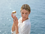 Woman gazing down toward the ocean holding a jar of white and gold Perles Des Mers 