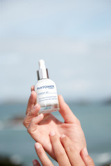 A woman holding the Pigment 2d Serum at the beach.
