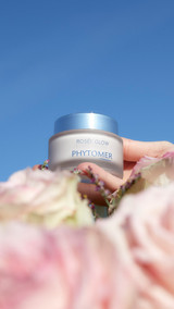 Rosee Glow Cream sitting on a table at the beach with it's lid off, displaying the pink creamy texture.