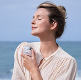 Woman holding Rosee Glow Cream close to her chest at the beach.