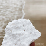 Close-up of white textured sea salt (Oligomer) held between fingers