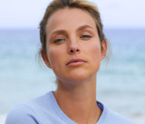 Woman looking into the camera with an ocean behind her.