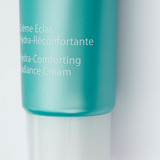 Close-up of a turquoise cosmetic tube showing "Crème Éclat Hydra-Réconfortante" and "Hydra-Comforting Radiance Cream" text.