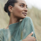 Woman in sage green sweater looking thoughtfully to the side with natural lighting.