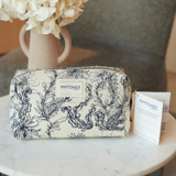 Phytomer cosmetic bag with botanical print design next to white flowers in a vase.