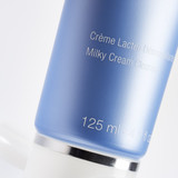 Blue skincare bottle showing "Crème Lactée Démaquillante Milky Cream Cleanser 125 ml" text.