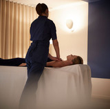 Massage therapist performing a treatment on a client lying on a massage table in a softly lit spa room with curtains.