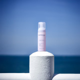 Pink Rose Visage Cleansing Foam sitting on a cement post with the ocean behind it.
