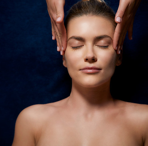 Woman with closed eyes receiving professional head and temple massage against dark blue background. Woman with closed eyes receiving professional head and temple massage against dark blue background.