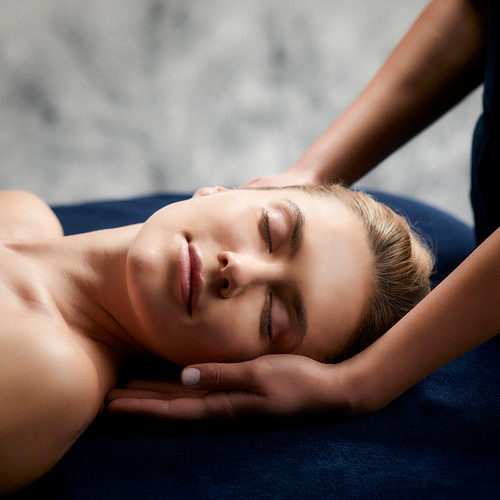 Woman with eyes closed receiving relaxing facial massage or spa treatment on blue towel.