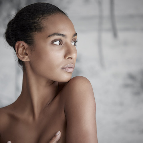 Woman with slicked-back hair and natural makeup looking to the side against blurred background. Woman with slicked-back hair and natural makeup looking to the side against blurred background.
