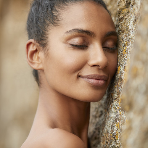 Woman with closed eyes and serene expression leaning against textured stone wall in natural lighting. Woman with closed eyes and serene expression leaning against textured stone wall in natural lighting.