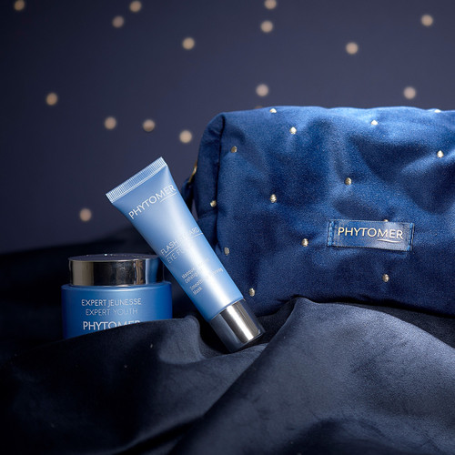 Phytomer skincare products including Expert Youth Cream and Eye Flash Mask displayed with an elegant navy cosmetic bag with gold dots against a starry night background. Phytomer skincare products including Expert Youth Cream and Eye Flash Mask displayed with an elegant navy cosmetic bag with gold dots against a starry night background.